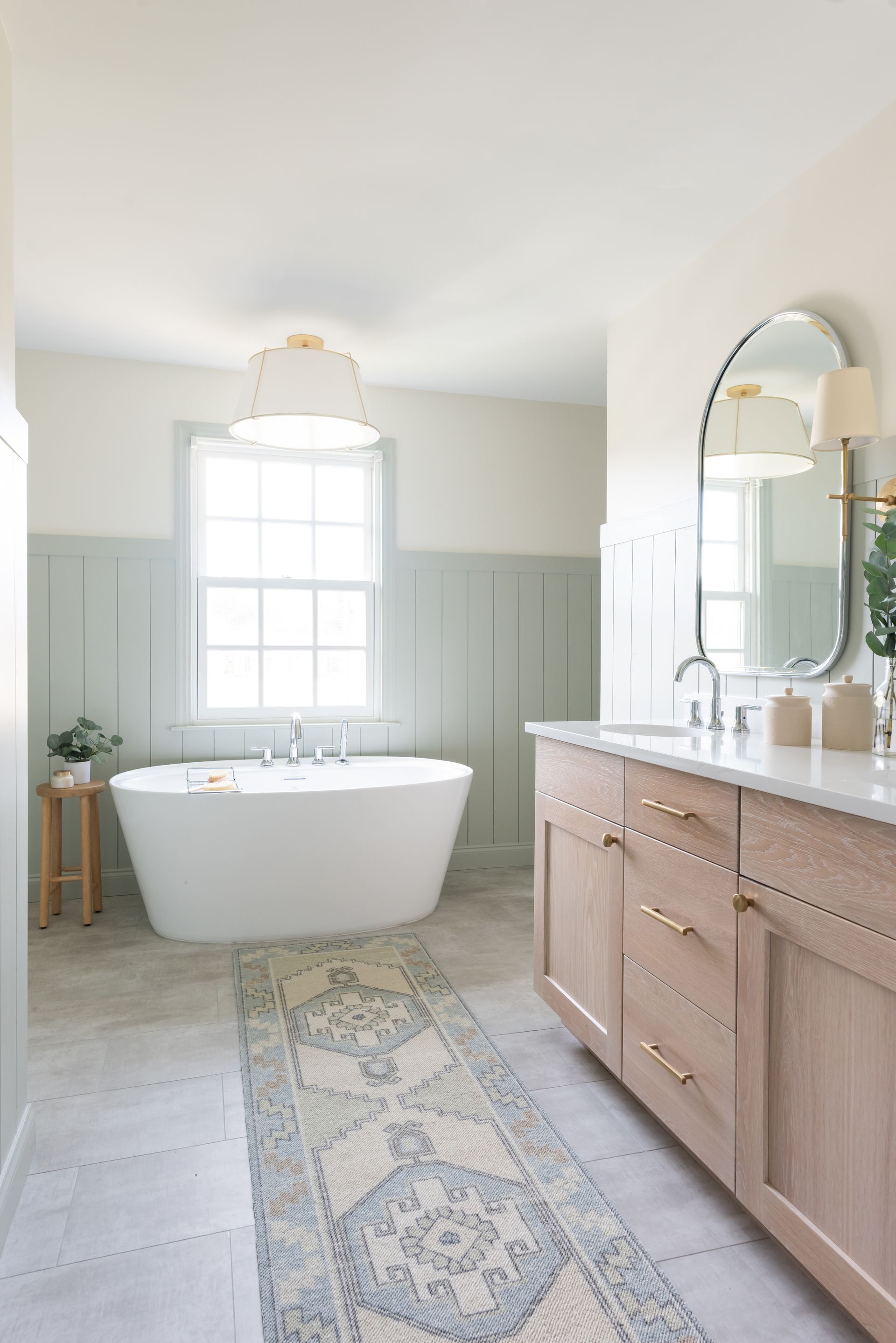 Elegant, light-toned bathroom with a freestanding tub, light wood vanity, and a patterned runner rug.