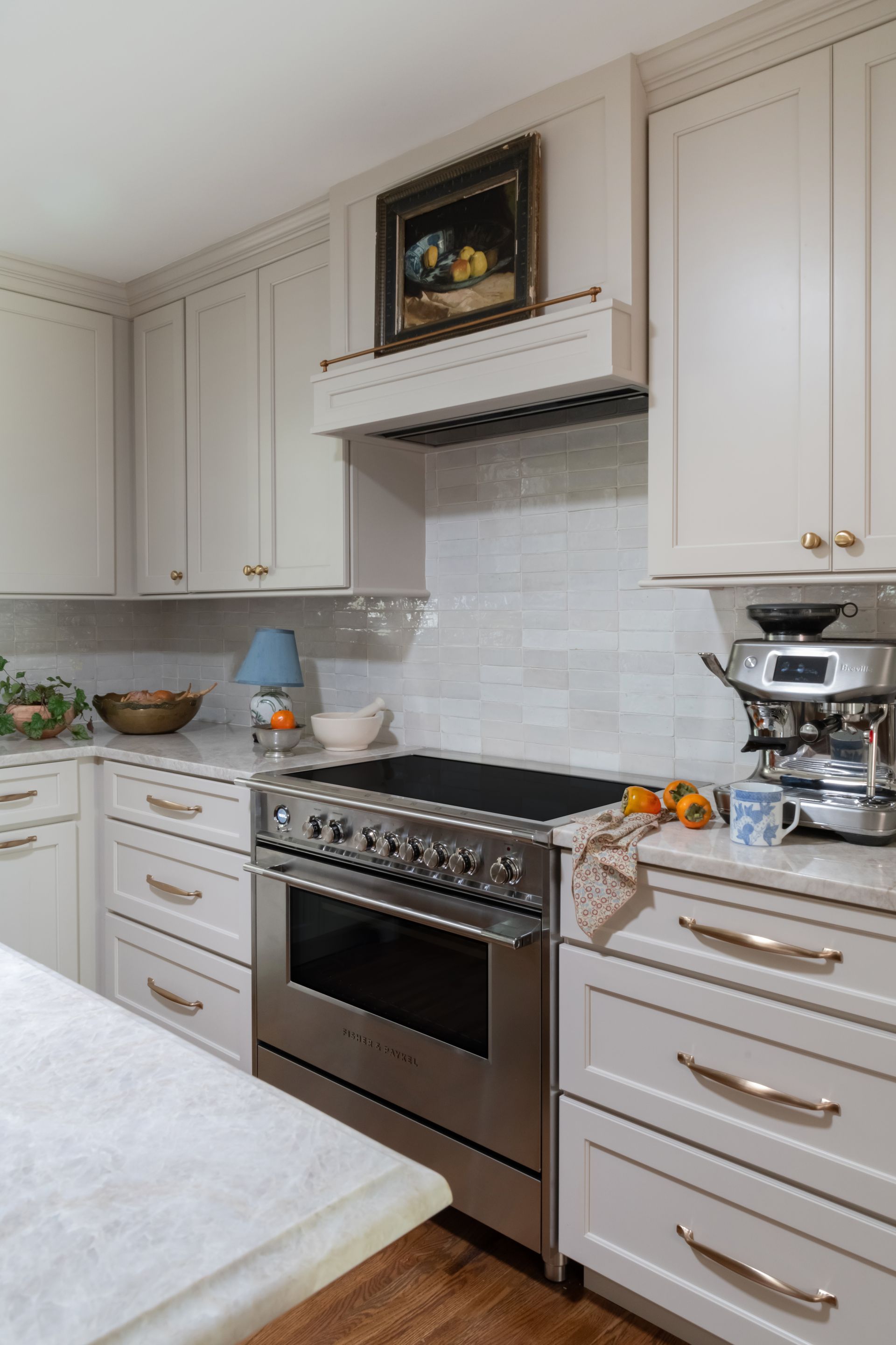 Cream-colored kitchen with stainless steel stove, cabinets, and range hood. A painting hangs above the stove.