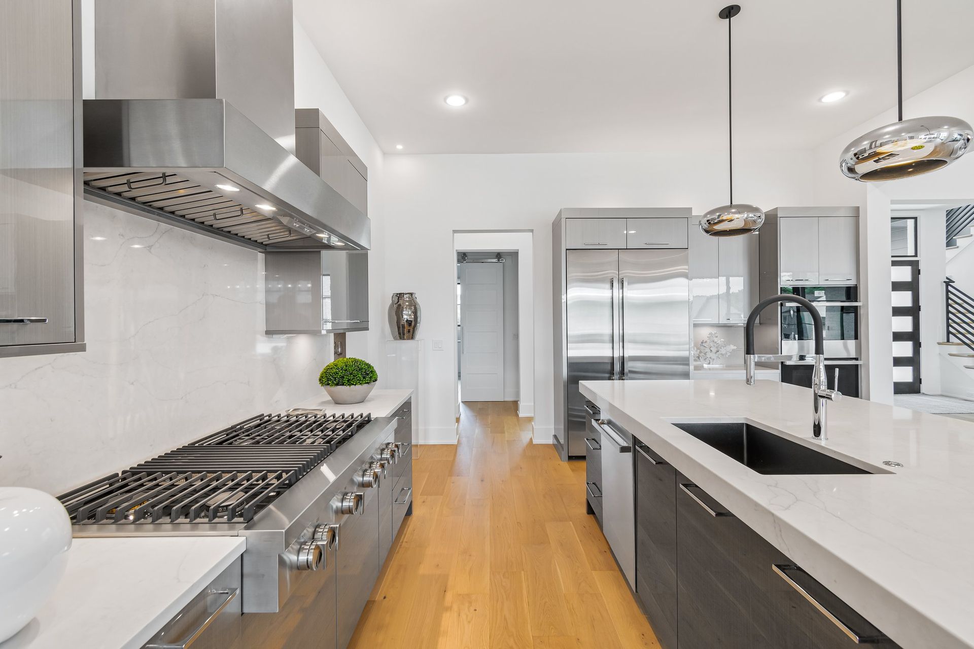 Modern kitchen with stainless steel appliances, light wood floors, and white countertops.
