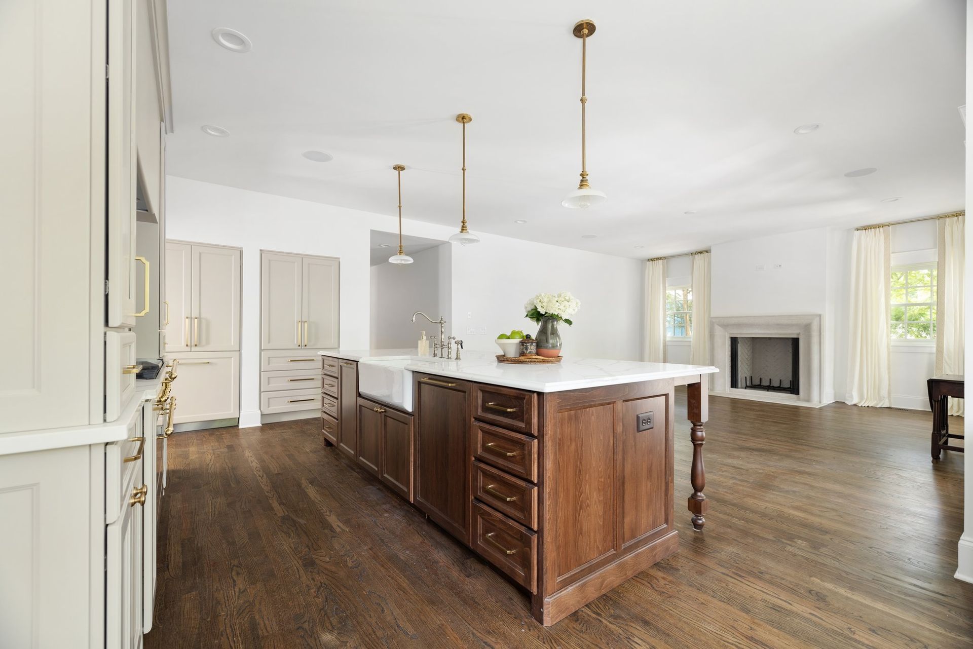 Kitchen with large wooden island, white countertops, three pendant lights, hardwood floors, and fireplace.