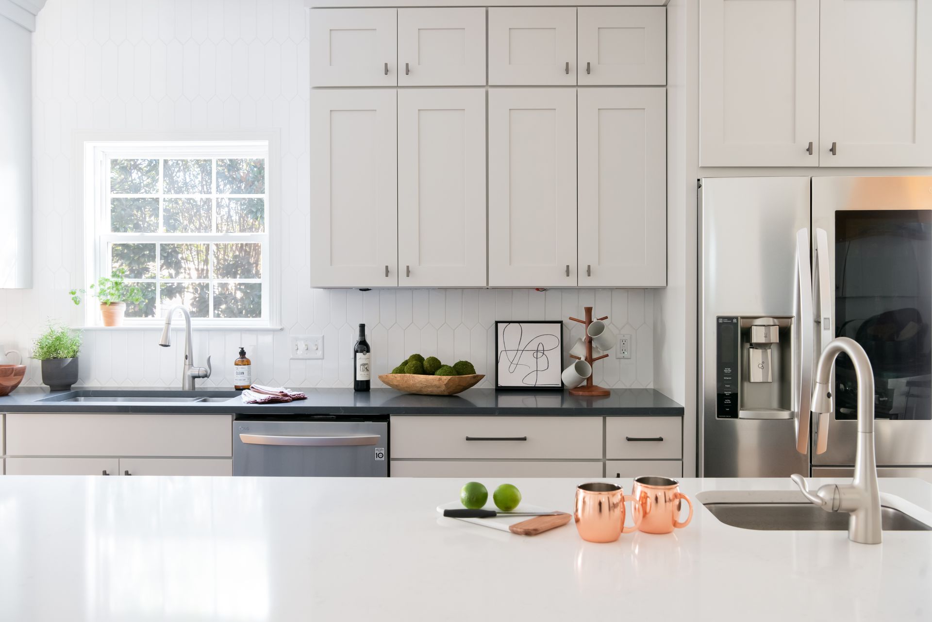 Modern kitchen with white countertops, gray cabinets, stainless steel appliances, and a window.
