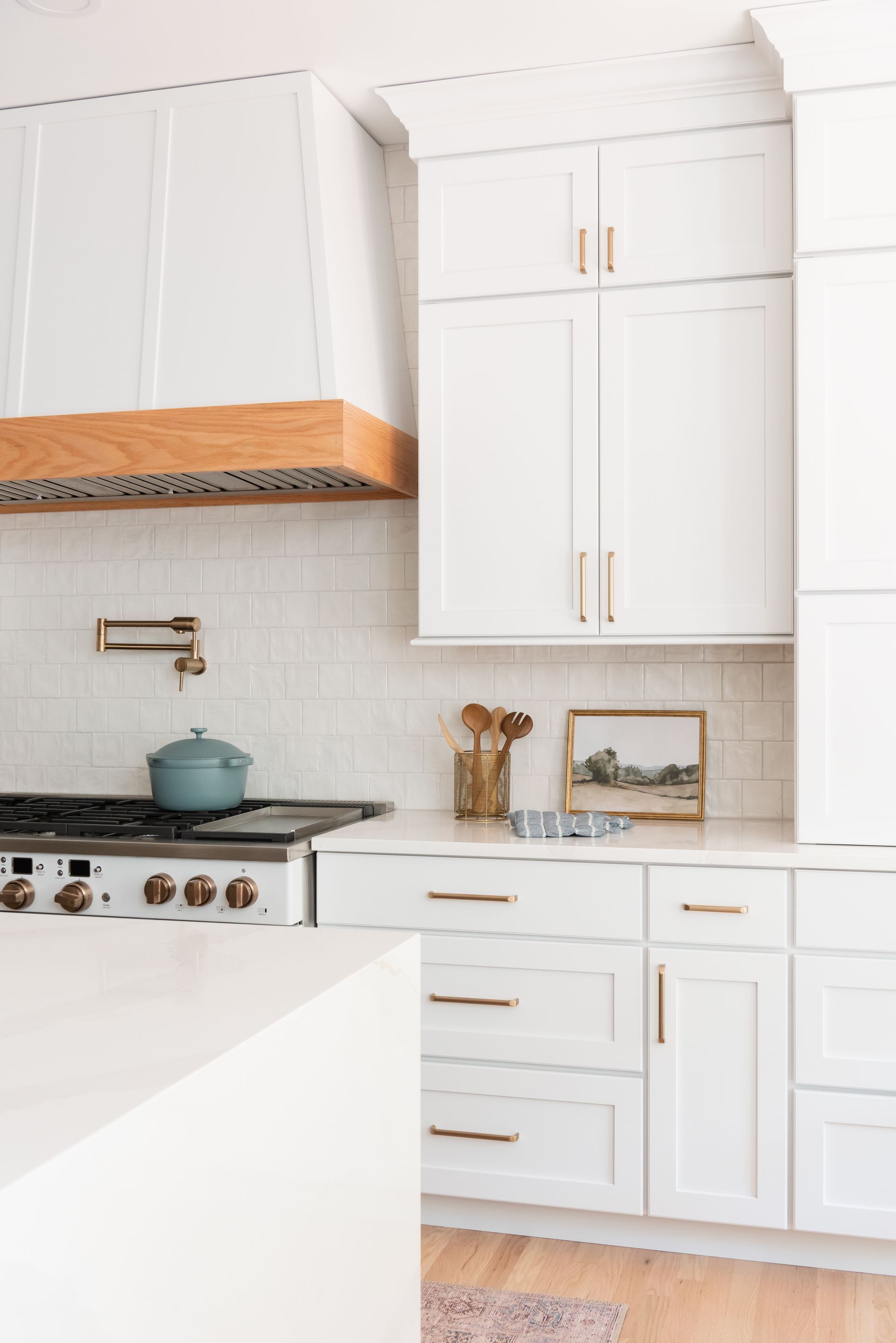White kitchen with wood accents, including a range hood, gold hardware, and blue accents.