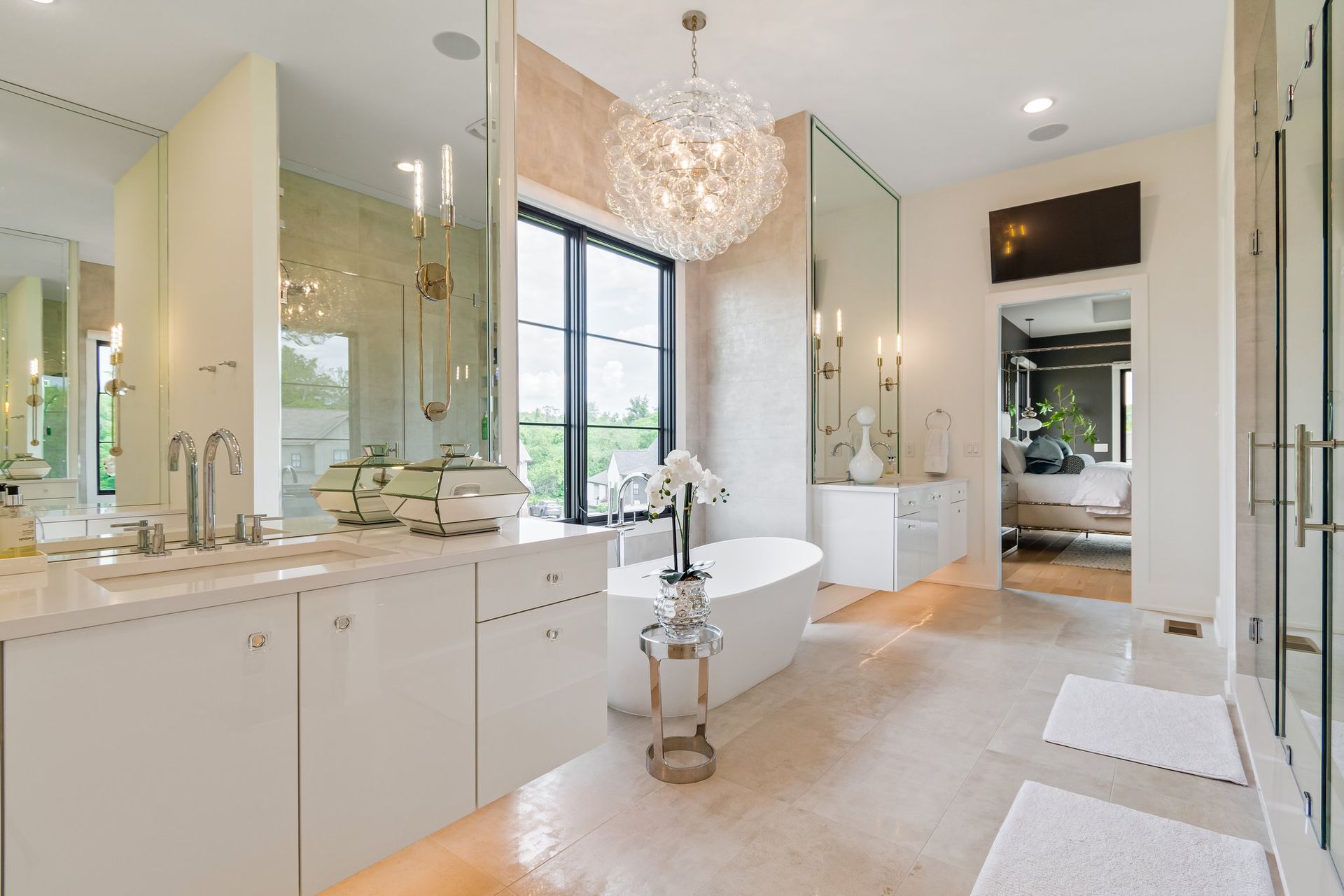 Luxurious white bathroom with a soaking tub, chandelier, and large mirrors.