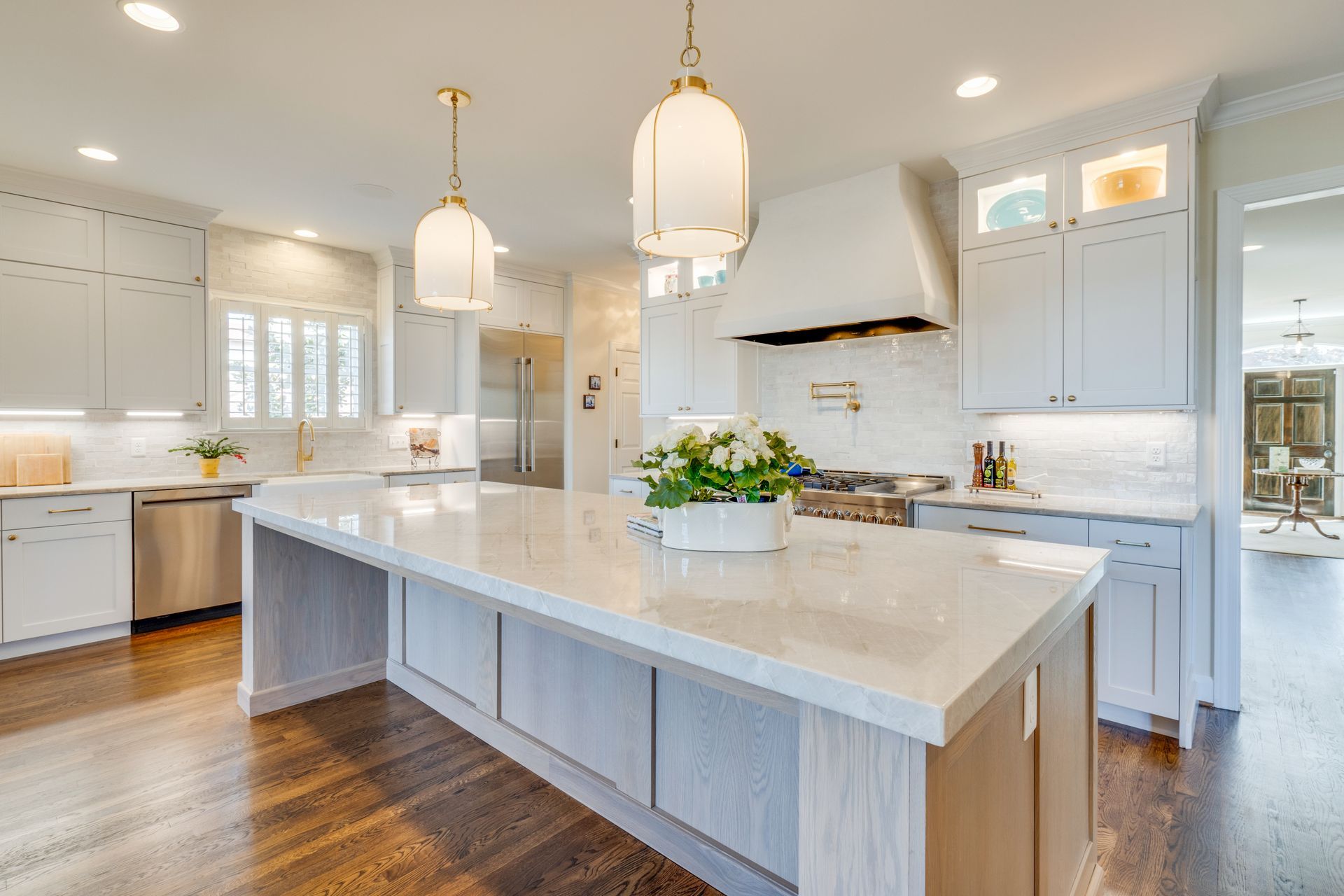 Spacious, modern kitchen with white cabinetry, large island, pendant lights, and stainless steel appliances.