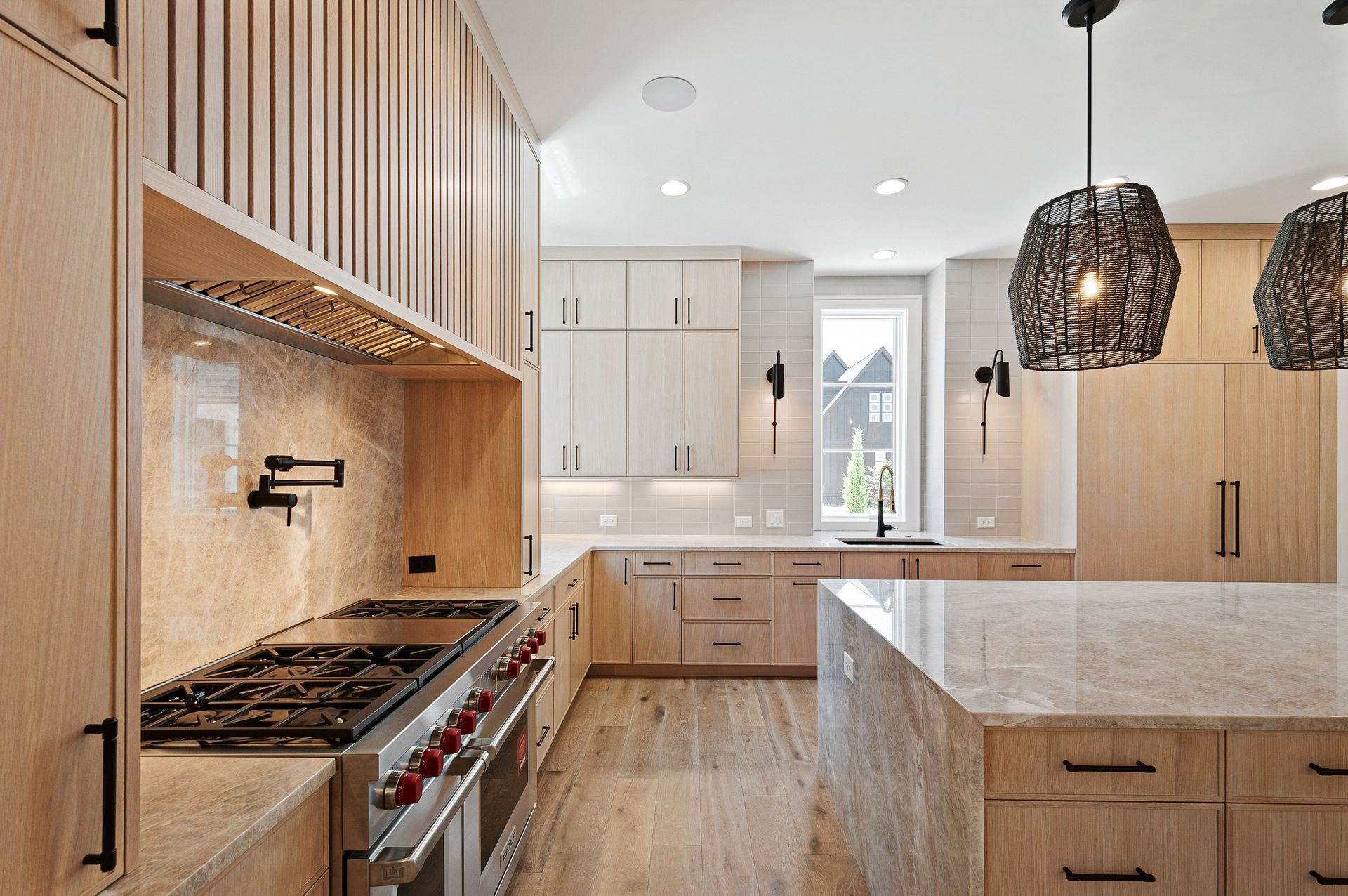 Modern kitchen with light wood cabinets, granite island, and pendant lights.
