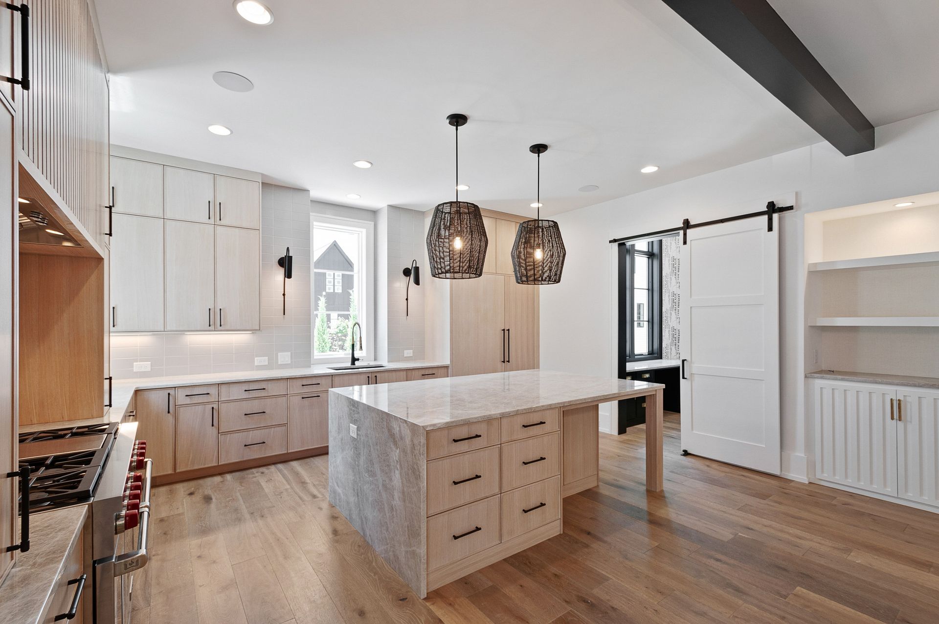 Modern kitchen with light wood cabinets, marble island, and pendant lights.