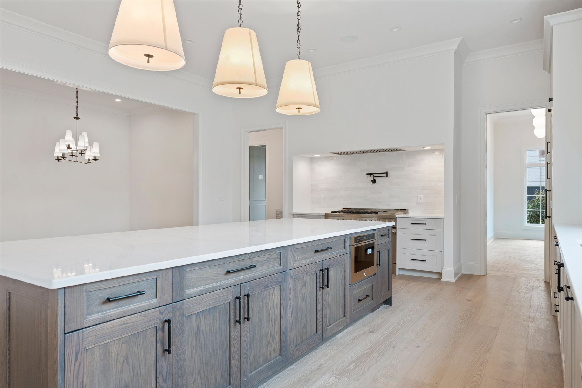 Modern kitchen with gray island, white countertops, three pendant lights, and light wood floors.