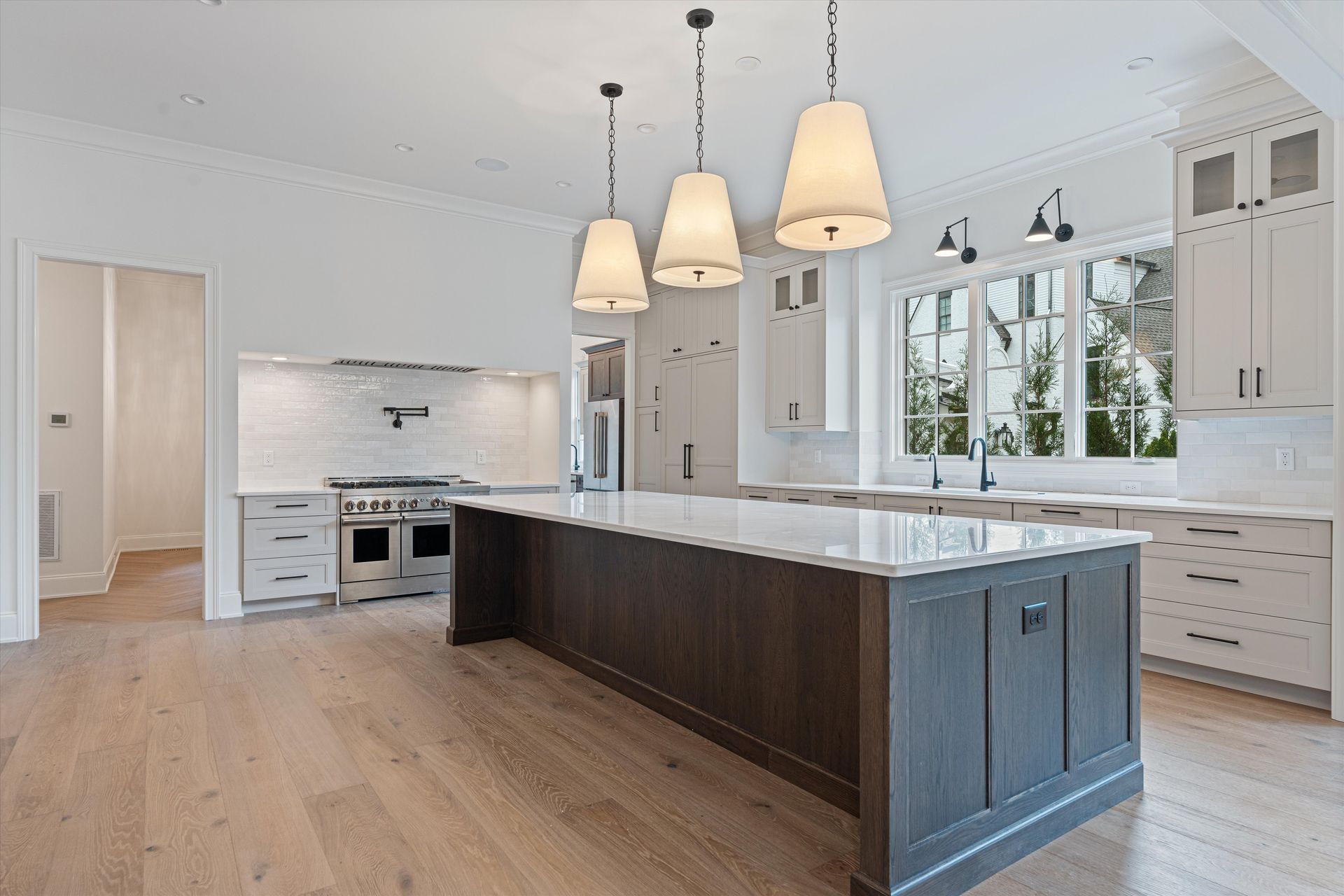 Modern white kitchen with dark island and light wood floor; three pendant lights hang above.