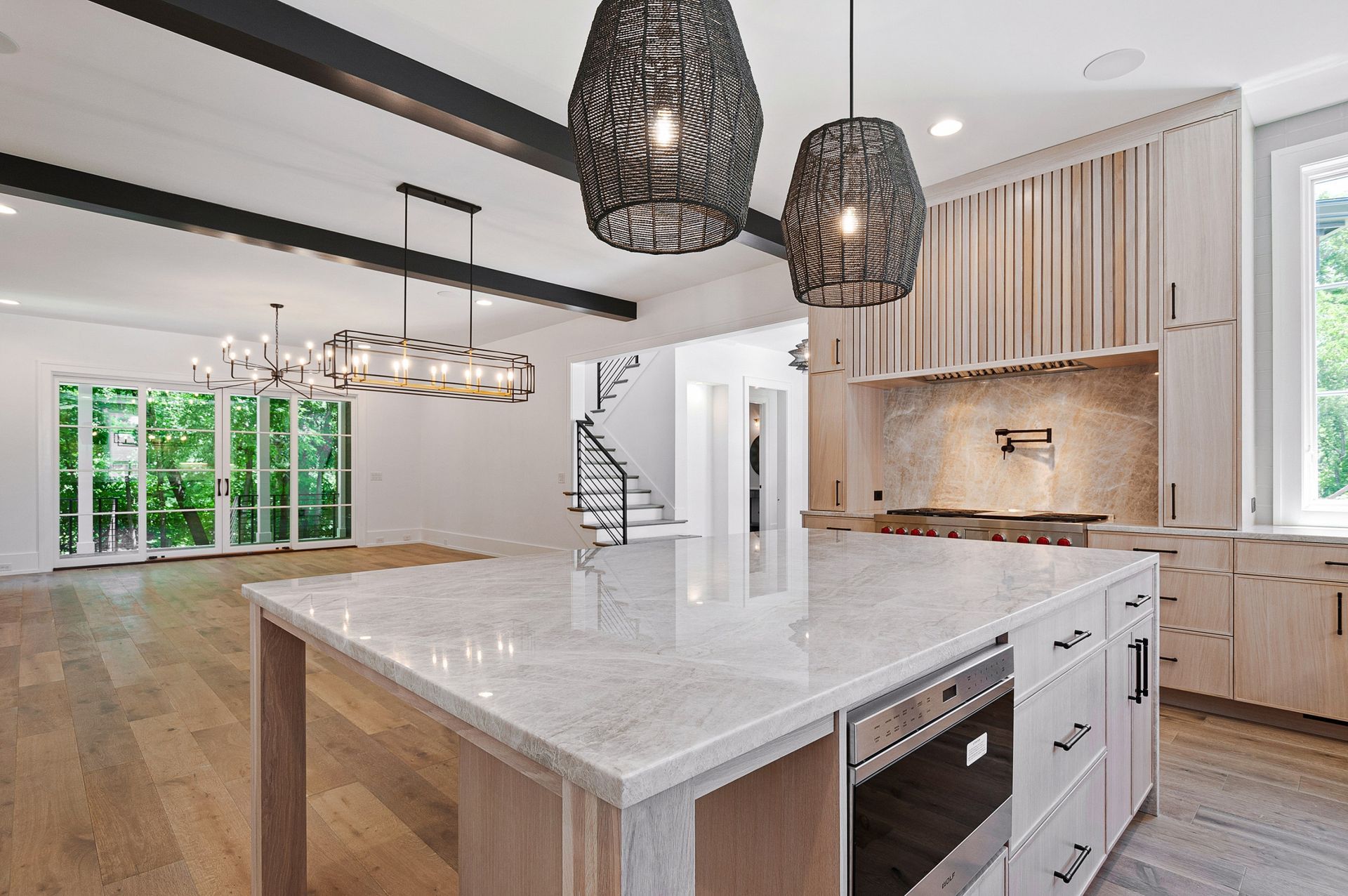 Spacious kitchen with island, pendant lights, wooden beams. Light wood cabinets and floor.