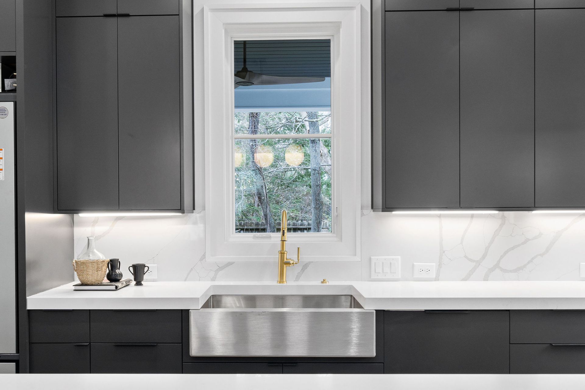 Modern kitchen with dark gray cabinets, stainless steel sink, and a window with a view.