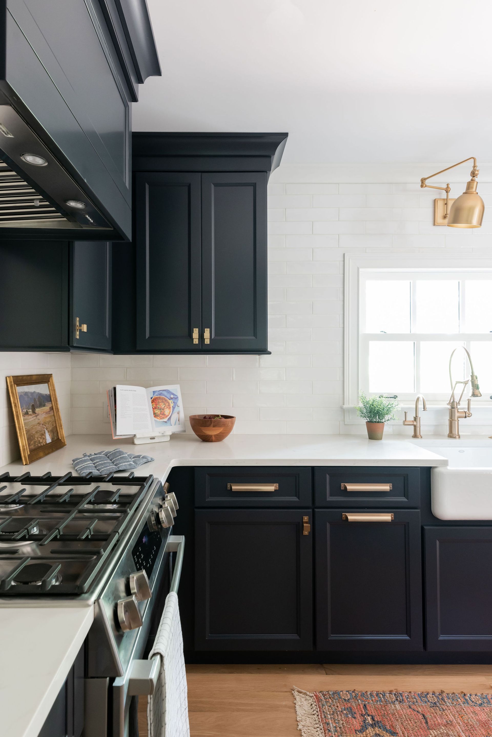 Black kitchen cabinets with gold hardware and white countertops, tile, and farmhouse sink.