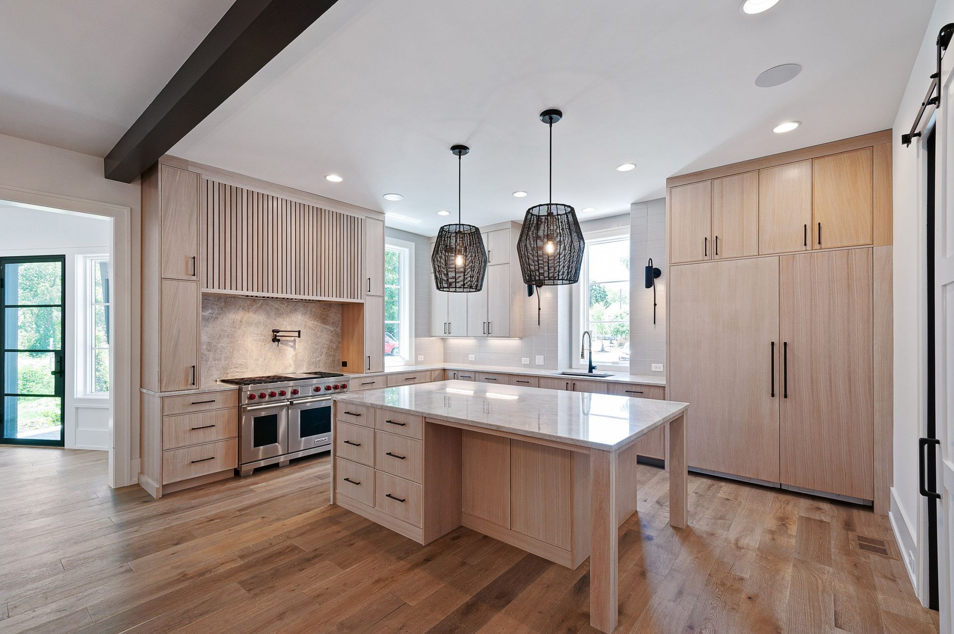Modern kitchen with light wood cabinets, marble island, stainless steel appliances, and two pendant lights.