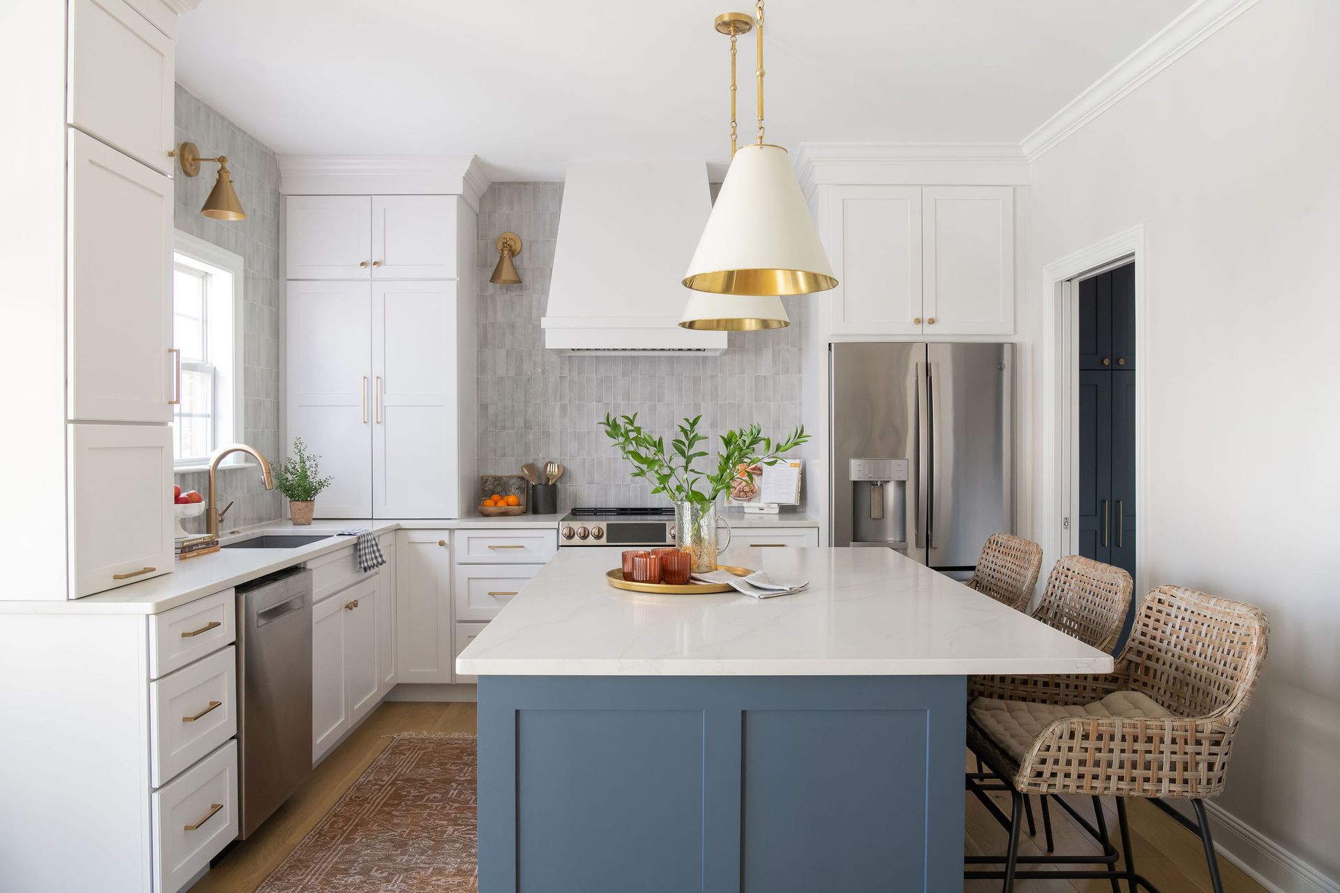 White kitchen with blue island and gold pendant lights.