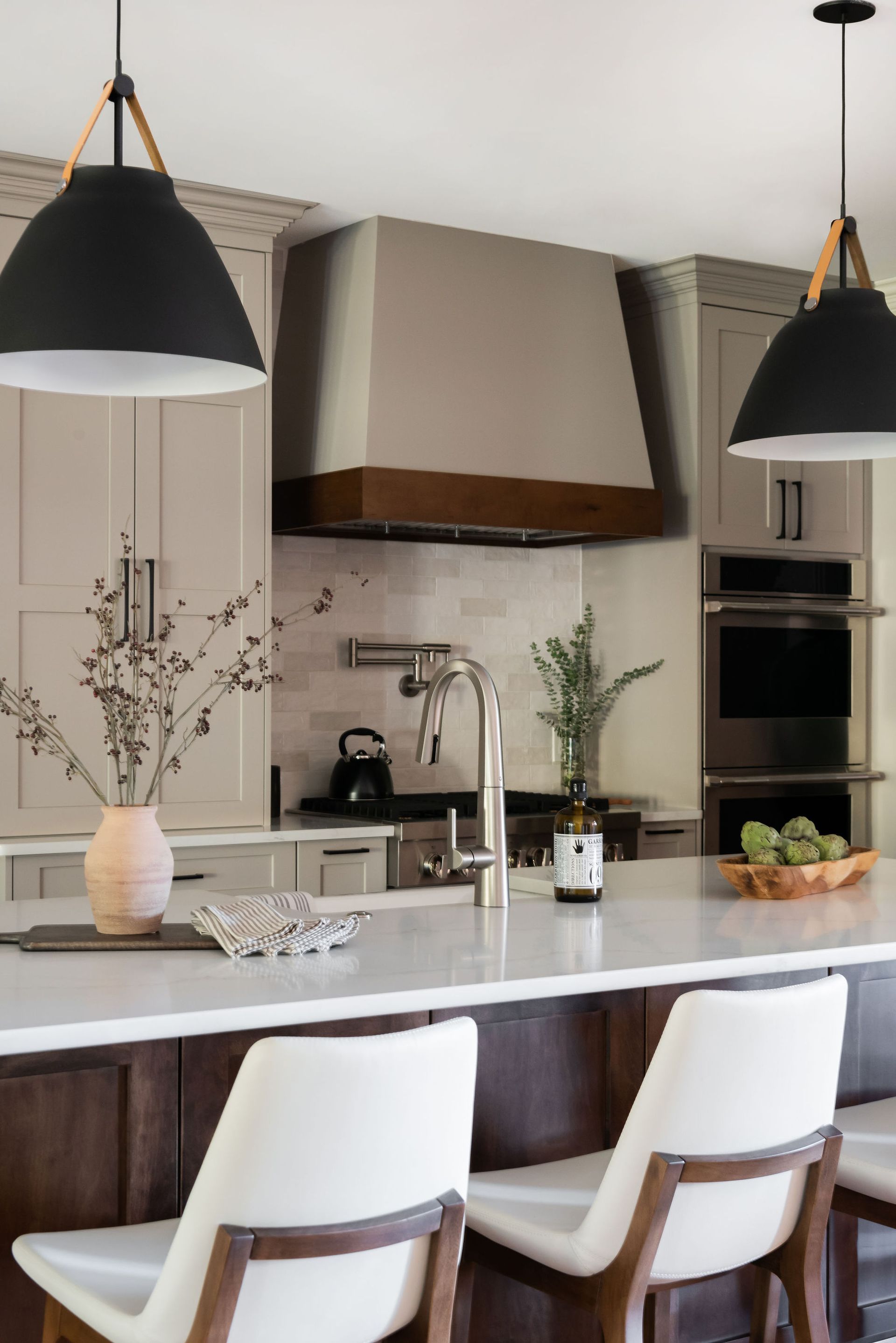 Modern kitchen with island, pendant lights, and stainless steel appliances. Beige cabinets, white countertops, and wood accents.