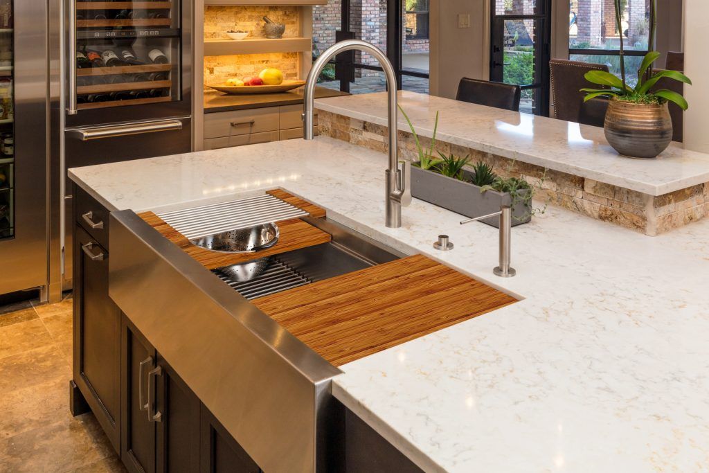 Modern kitchen island with stainless steel sink, wood drainer, and white countertop.