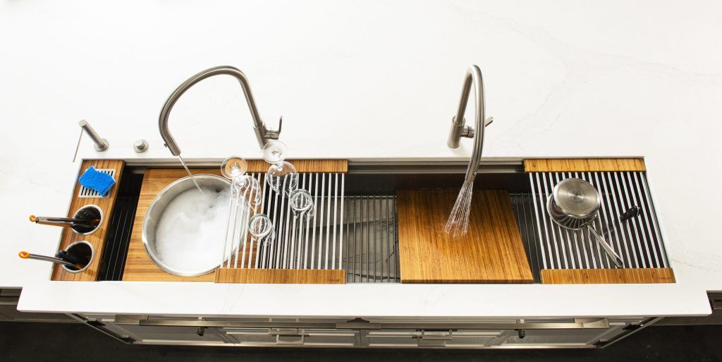 Overhead view of a kitchen sink with two faucets and integrated accessories, including cutting boards and drying racks.