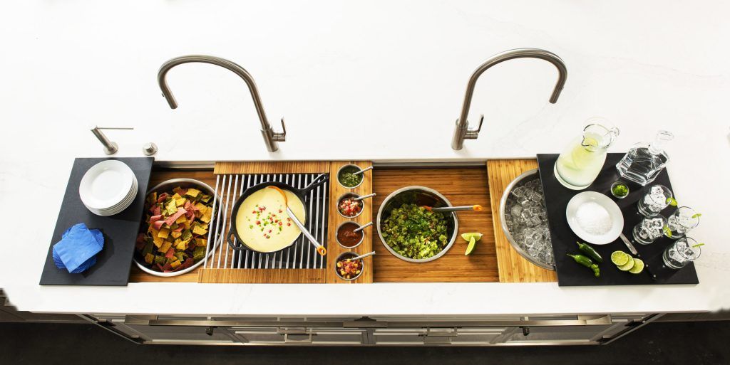 A sink with food and drinks arranged on wooden boards, including salsa, guacamole, and cocktails.