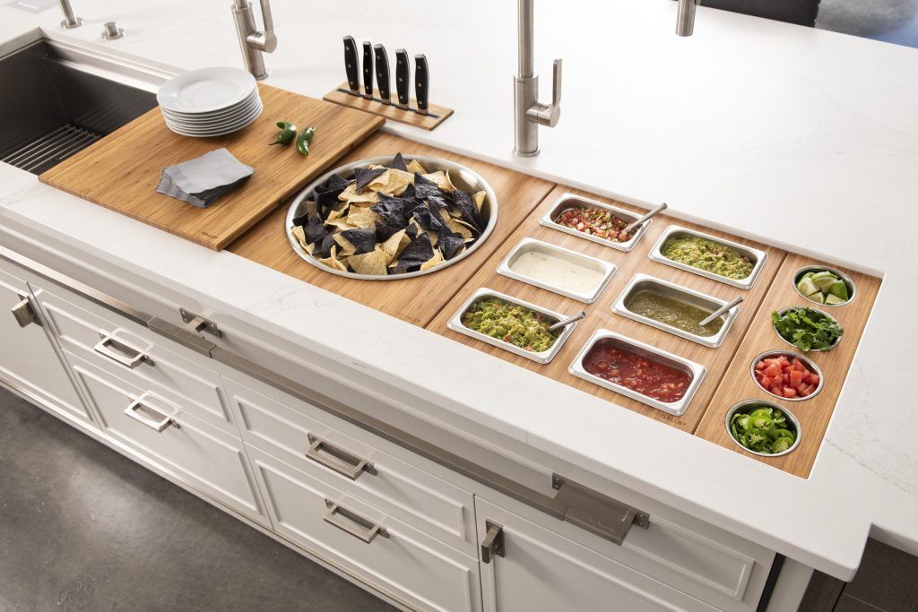 Kitchen countertop with integrated food prep station, including toppings and chips, beside a sink.