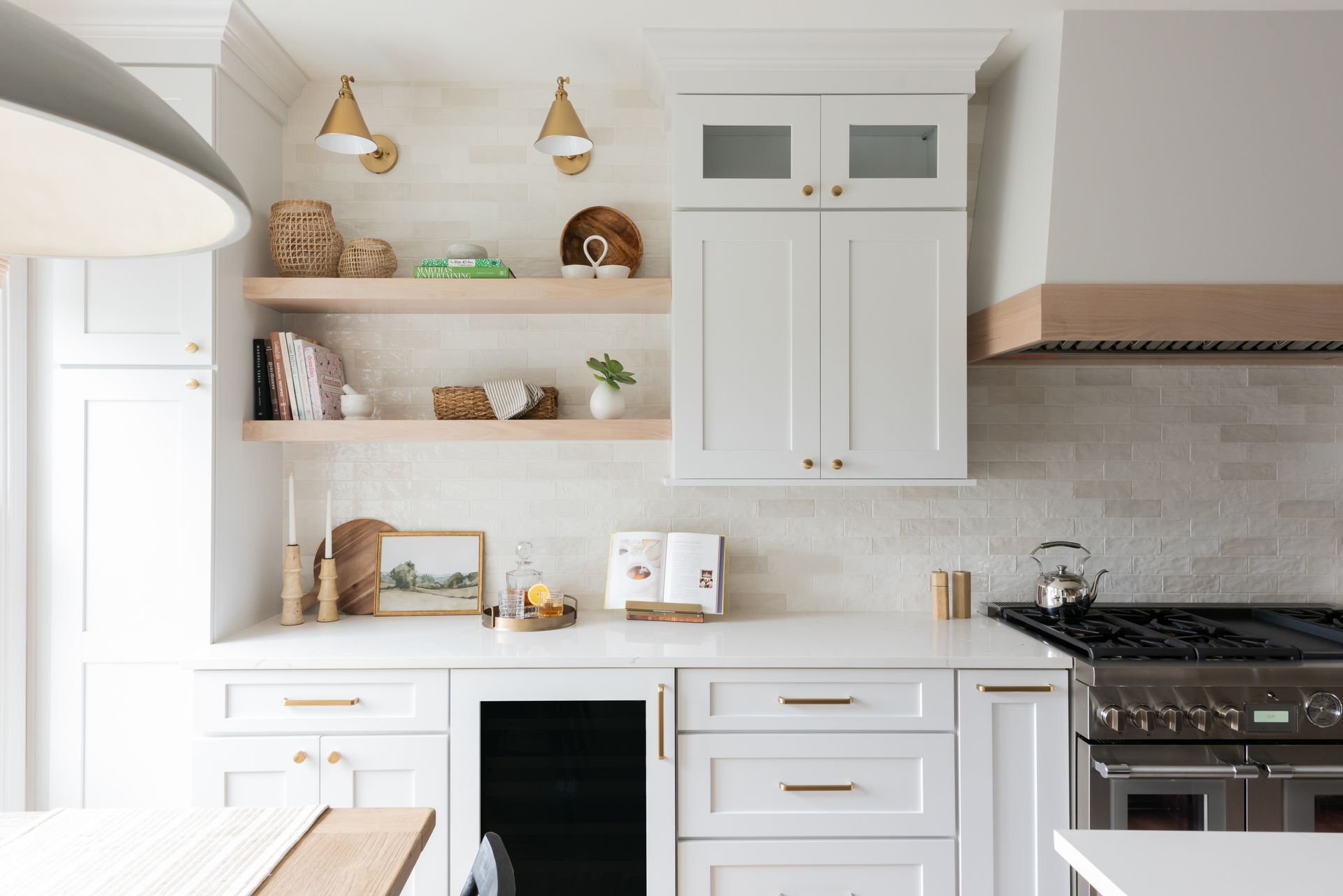 A bright, modern kitchen featuring white cabinets, light wood floating shelves, a brick backsplash, and a large range stove.