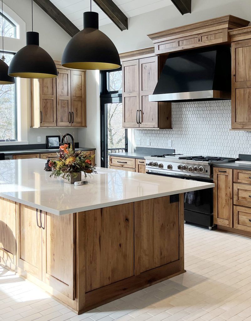Kitchen with wooden cabinets, island with light countertop, black pendant lights, and stainless steel appliances.