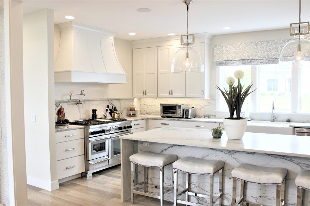 White kitchen with marble countertops, island with seating, stainless steel appliances, and pendant lights.