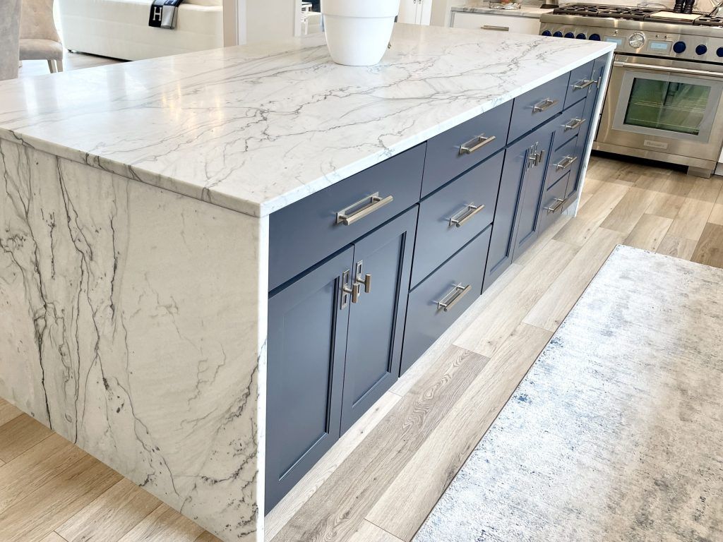 Kitchen island with gray cabinets and white countertop, with marble-like veining.