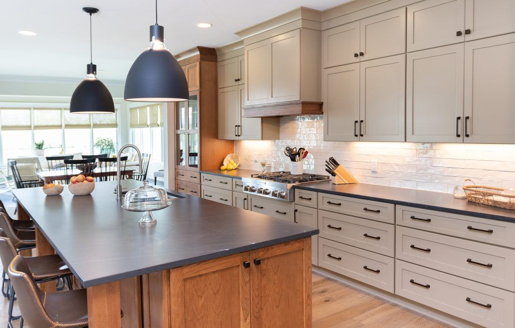 Modern kitchen with large island, beige cabinets, dark countertops, and pendant lights.