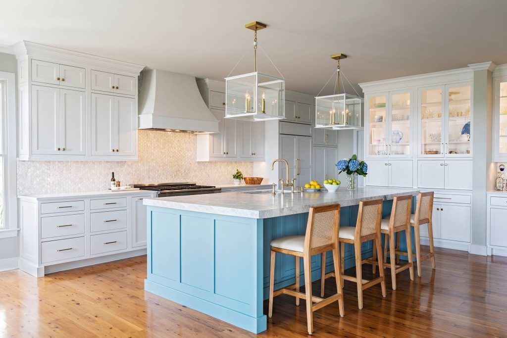 Bright blue kitchen island with white cabinets, gold light fixtures, and wooden stools.