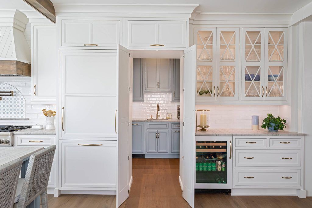 White kitchen with a hidden pantry, blue-grey cabinets, and a wine fridge.