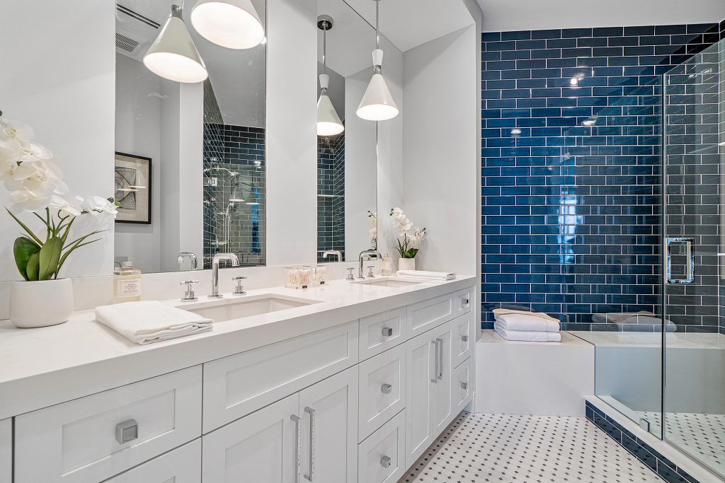 Bathroom with white cabinetry, blue tiled accent wall, and glass shower.