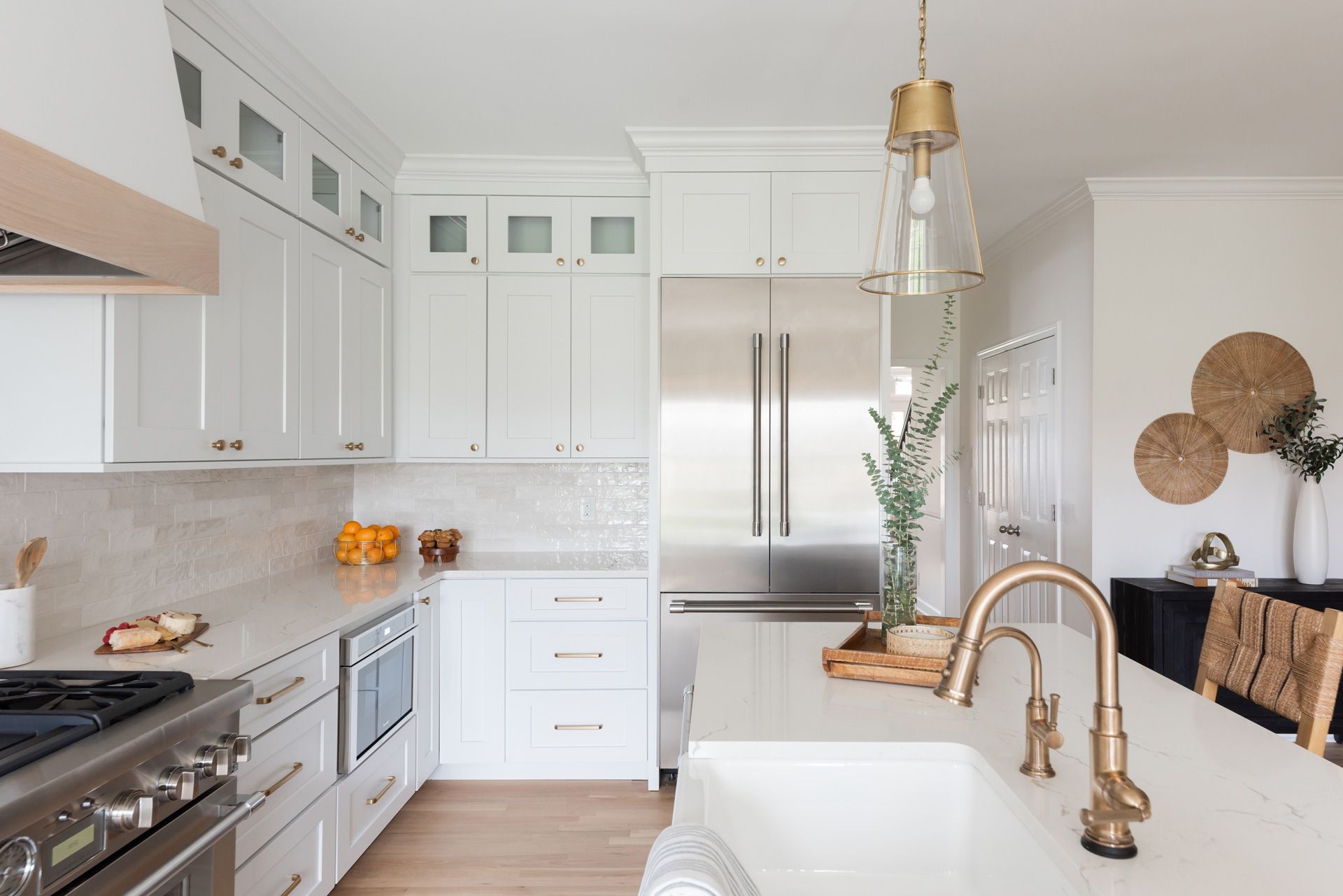 White kitchen with stainless steel appliances, marble countertop, gold faucet, and light fixture.