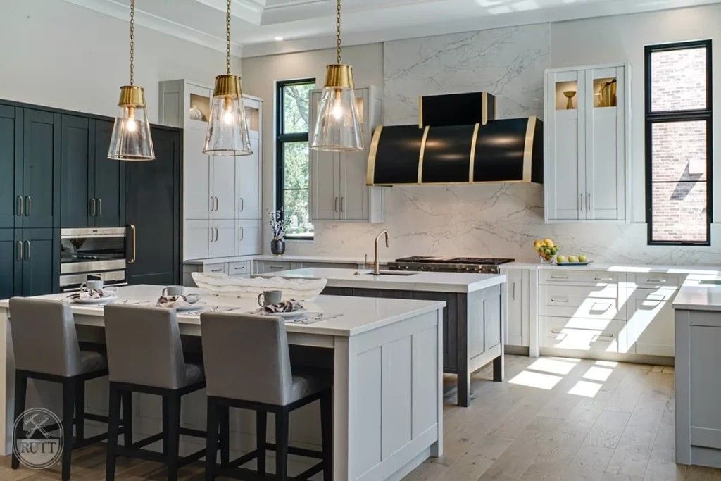 Modern kitchen with white and dark gray cabinets, island with stools, and gold light fixtures.