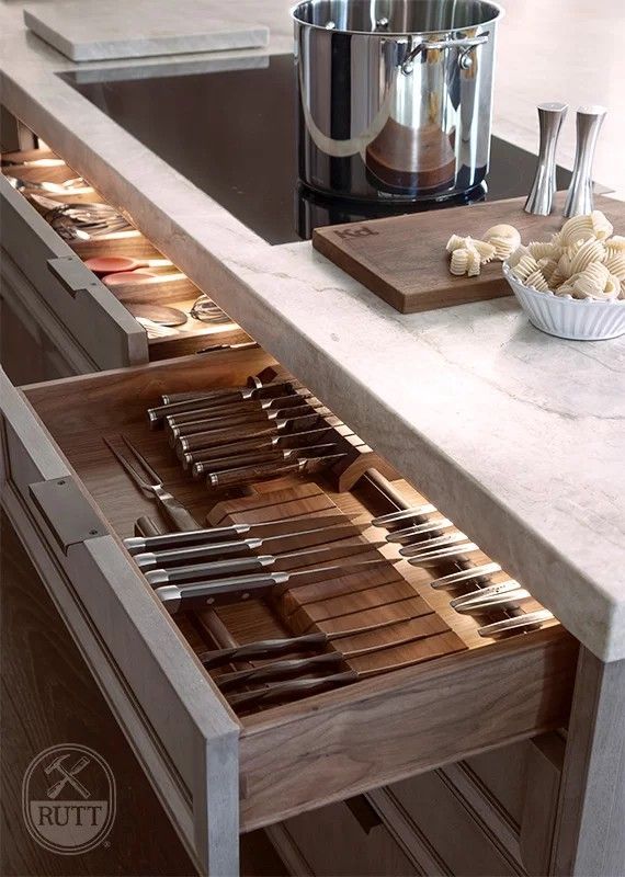 Open kitchen drawer with lit interior, holding silverware. Countertop with cooktop, pot, and food prep.