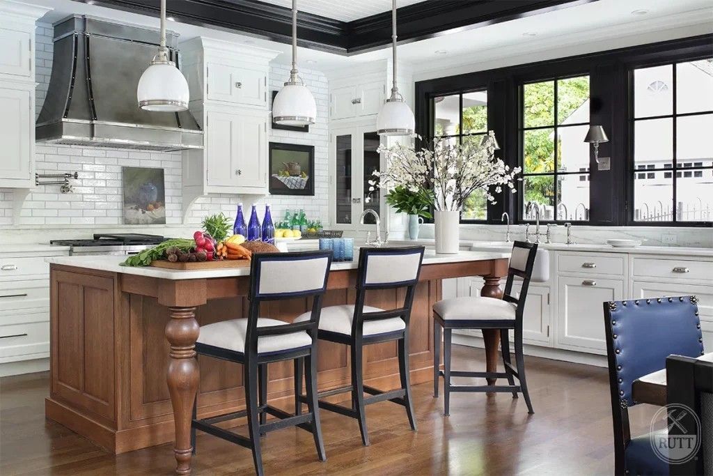 Kitchen with island, stainless steel hood, white cabinets, black-framed windows, bar stools.
