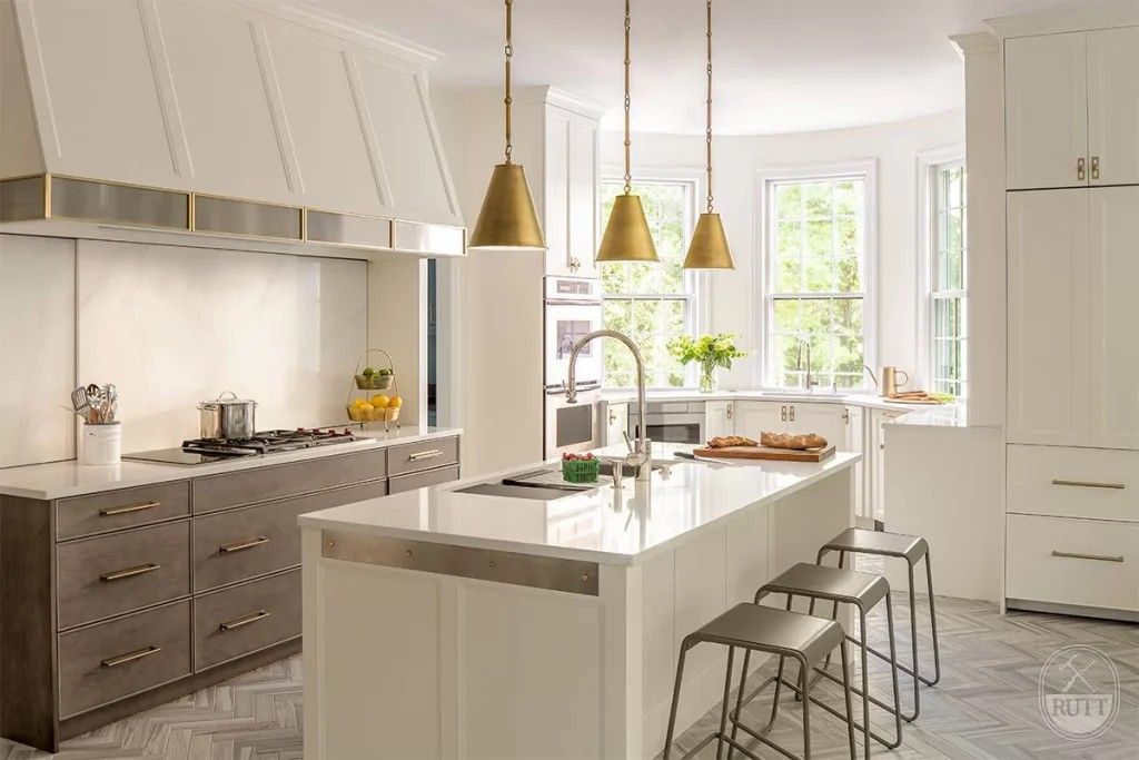 Modern kitchen with white island and cabinetry, gold pendant lights, and stainless steel range hood.