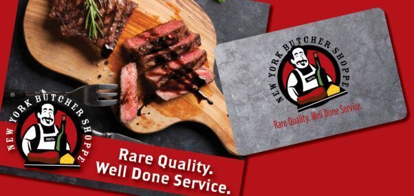 Sliced steak on a cutting board with a New York Butcher Shoppe gift card. Red background.