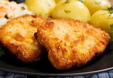 Breaded, fried chicken cutlets served with boiled potatoes and coleslaw on a black plate.
