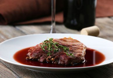 Steak with red wine sauce and thyme on a white plate; wine bottle and cork in the background.