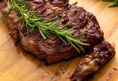 Close-up of grilled steak with rosemary garnish on a wooden cutting board.
