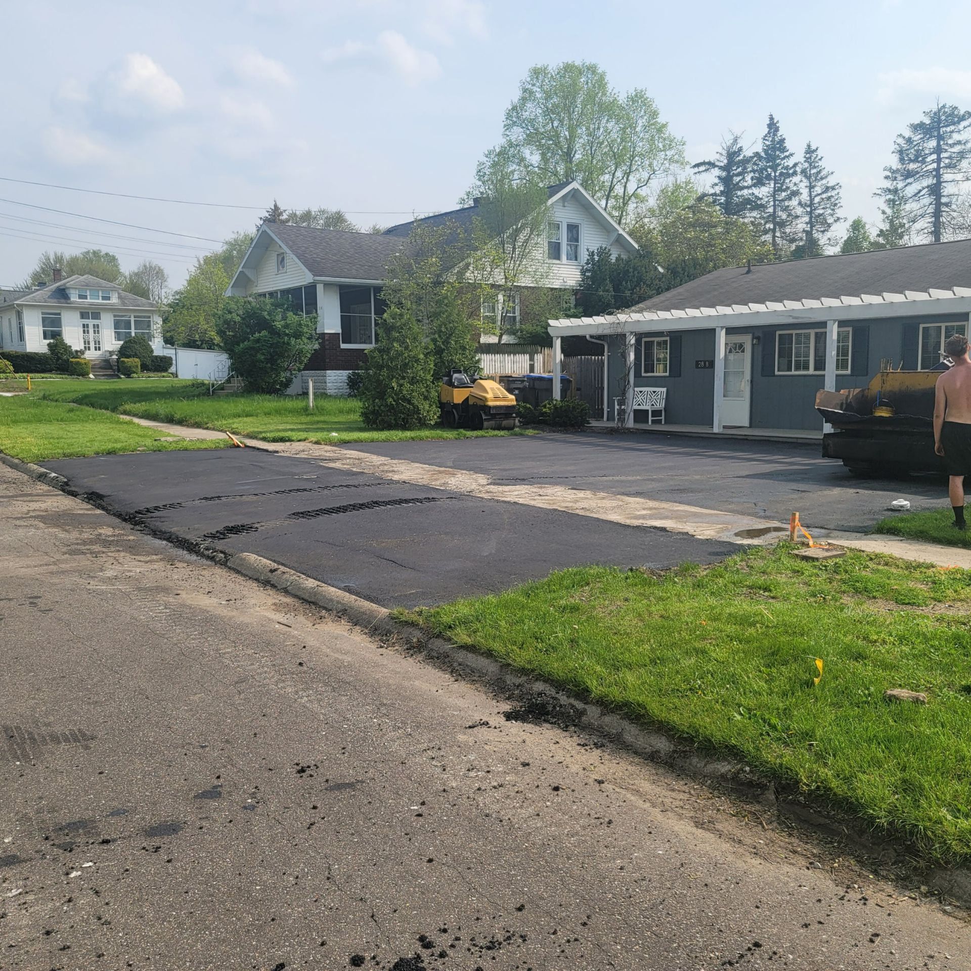 Residential driveway with fresh black paving, a gray house, and a yellow truck parked nearby.