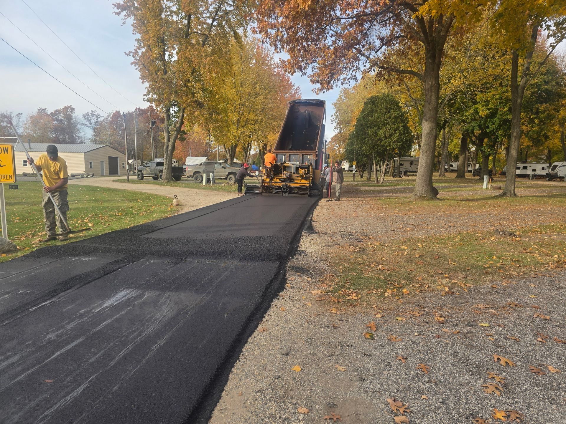 Road paving crew laying fresh asphalt on a tree-lined street in autumn