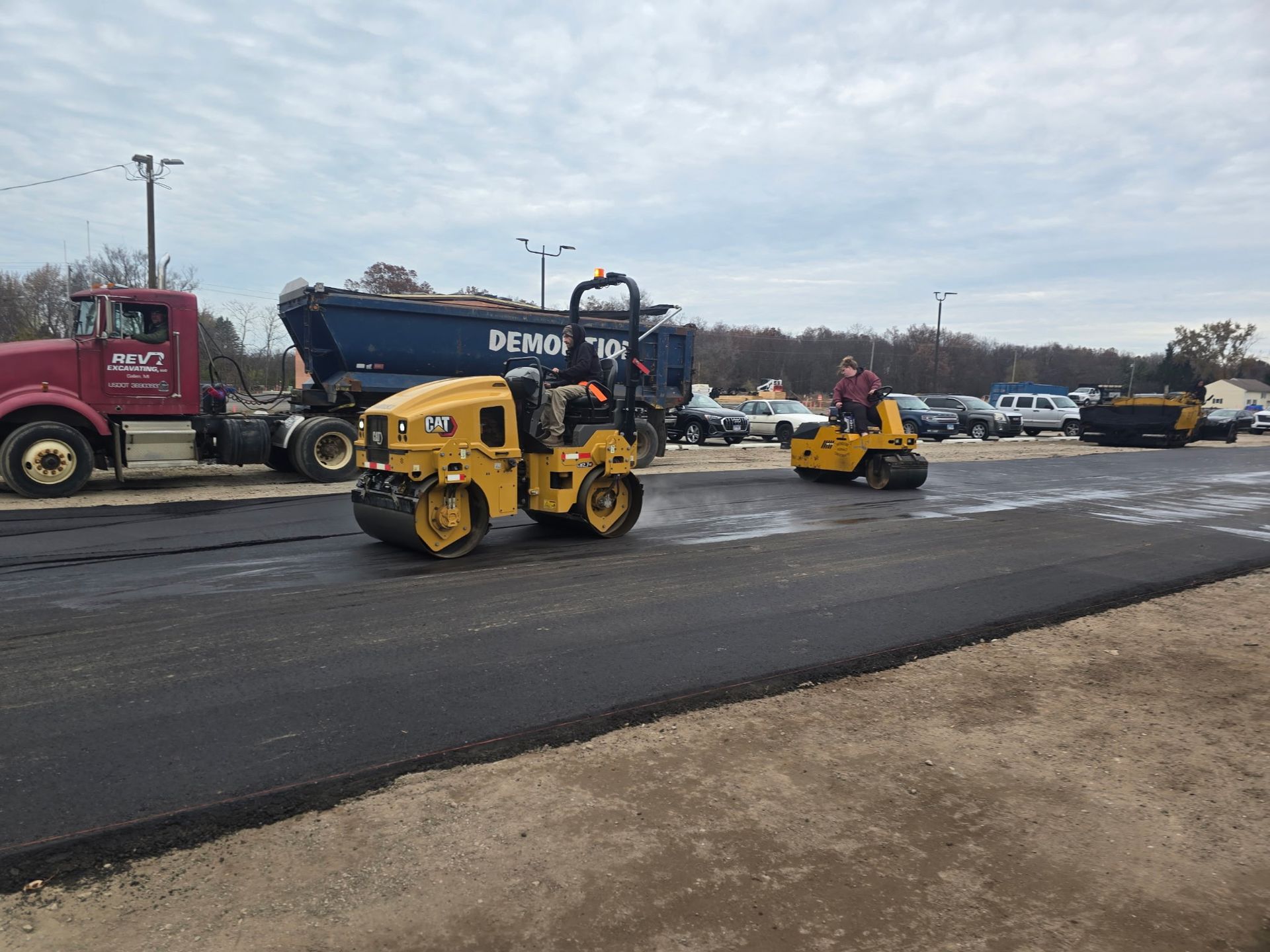 Road paving scene with yellow skid steers and a dump truck on a freshly resurfaced road