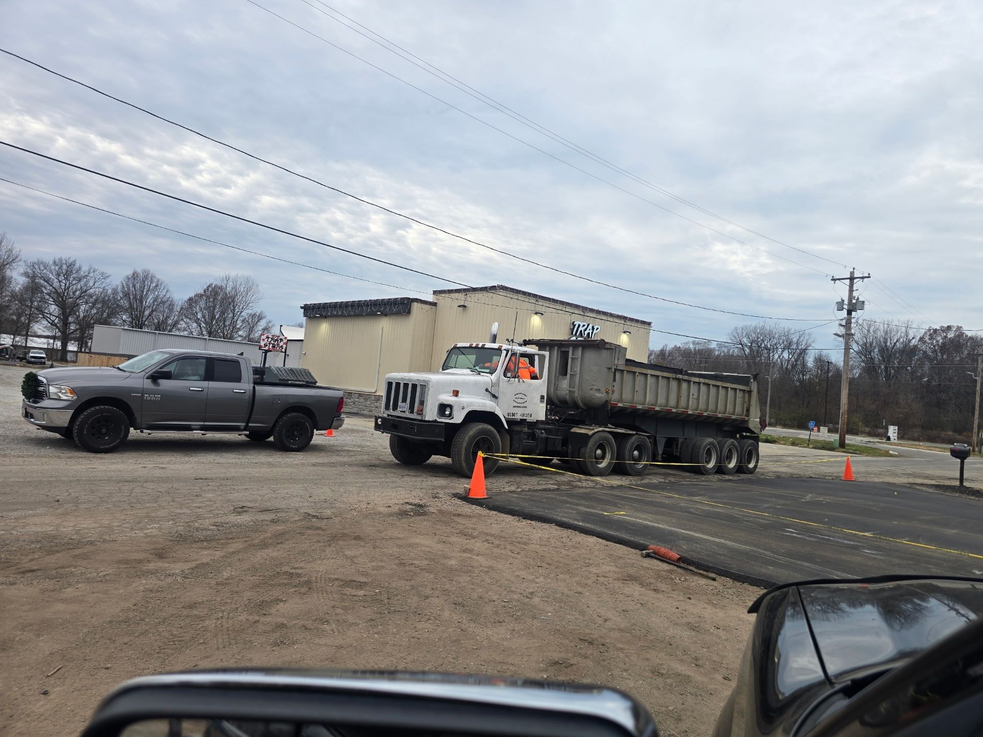 Tow truck and pickup at roadside incident, with traffic cones and utility lines under cloudy sky