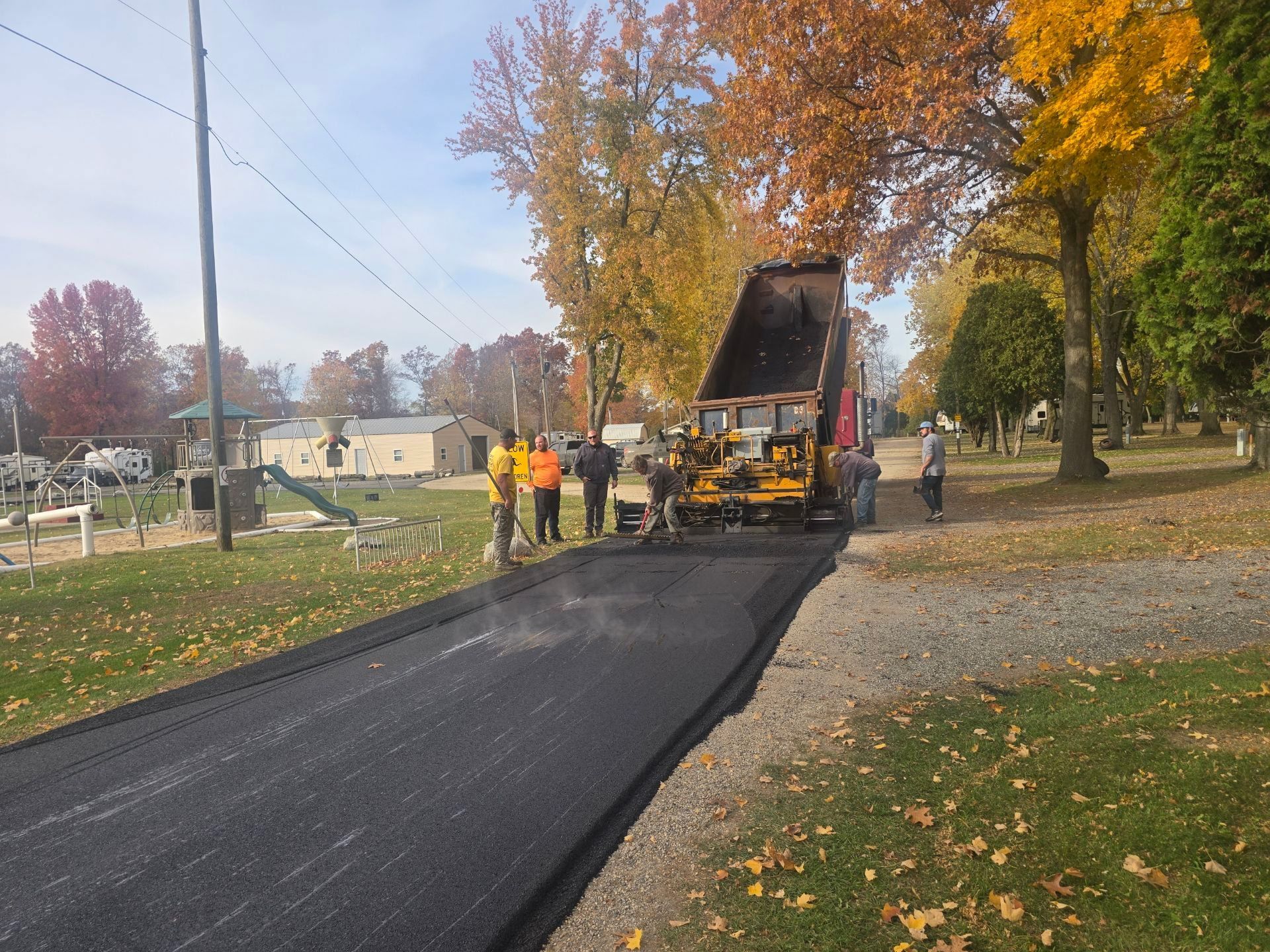 Road crew paving a residential street with fresh black asphalt in autumn.