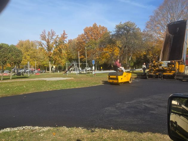 Road paving machine on a fresh blacktop road beside autumn trees under a blue sky