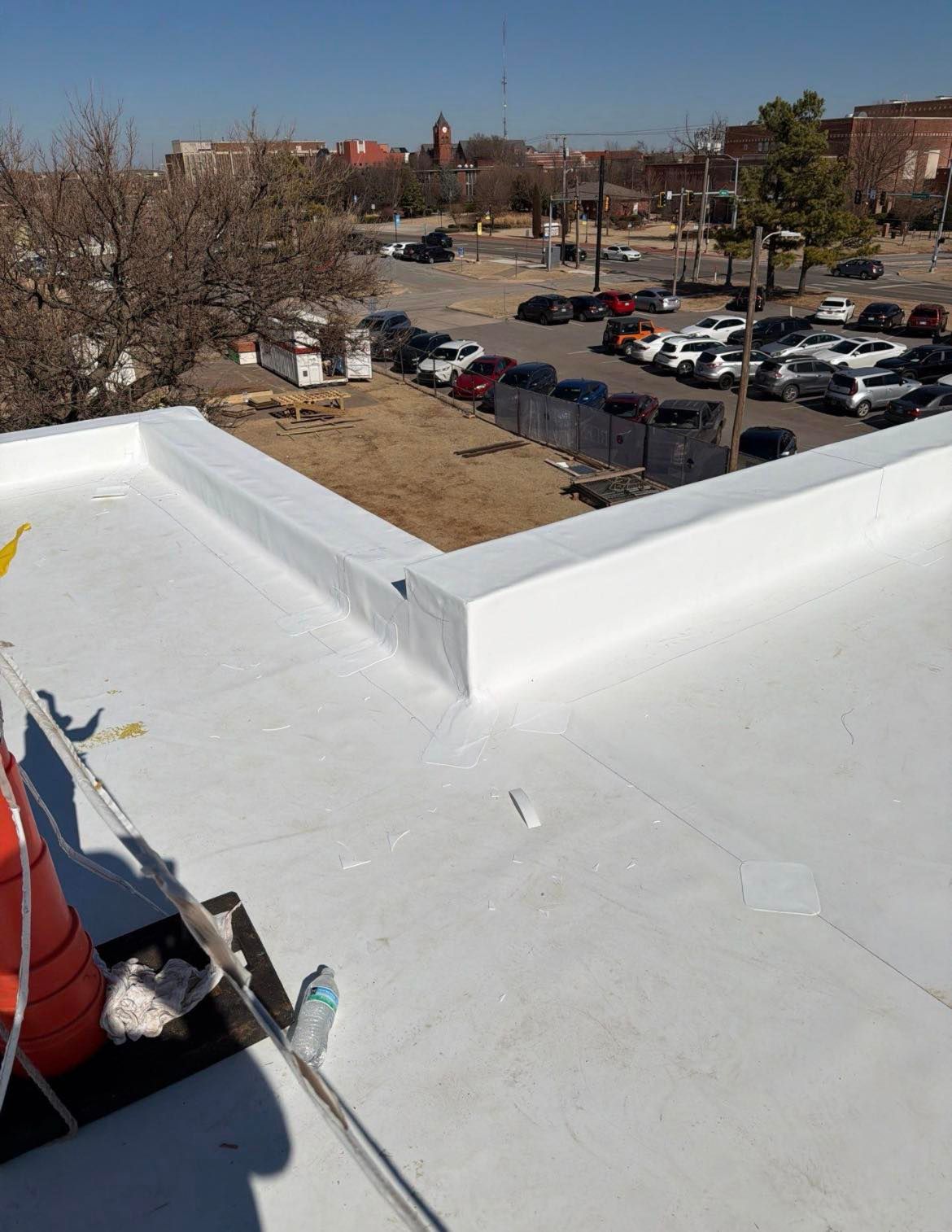 White coated flat roof with parapet, in urban setting. Cars parked nearby.