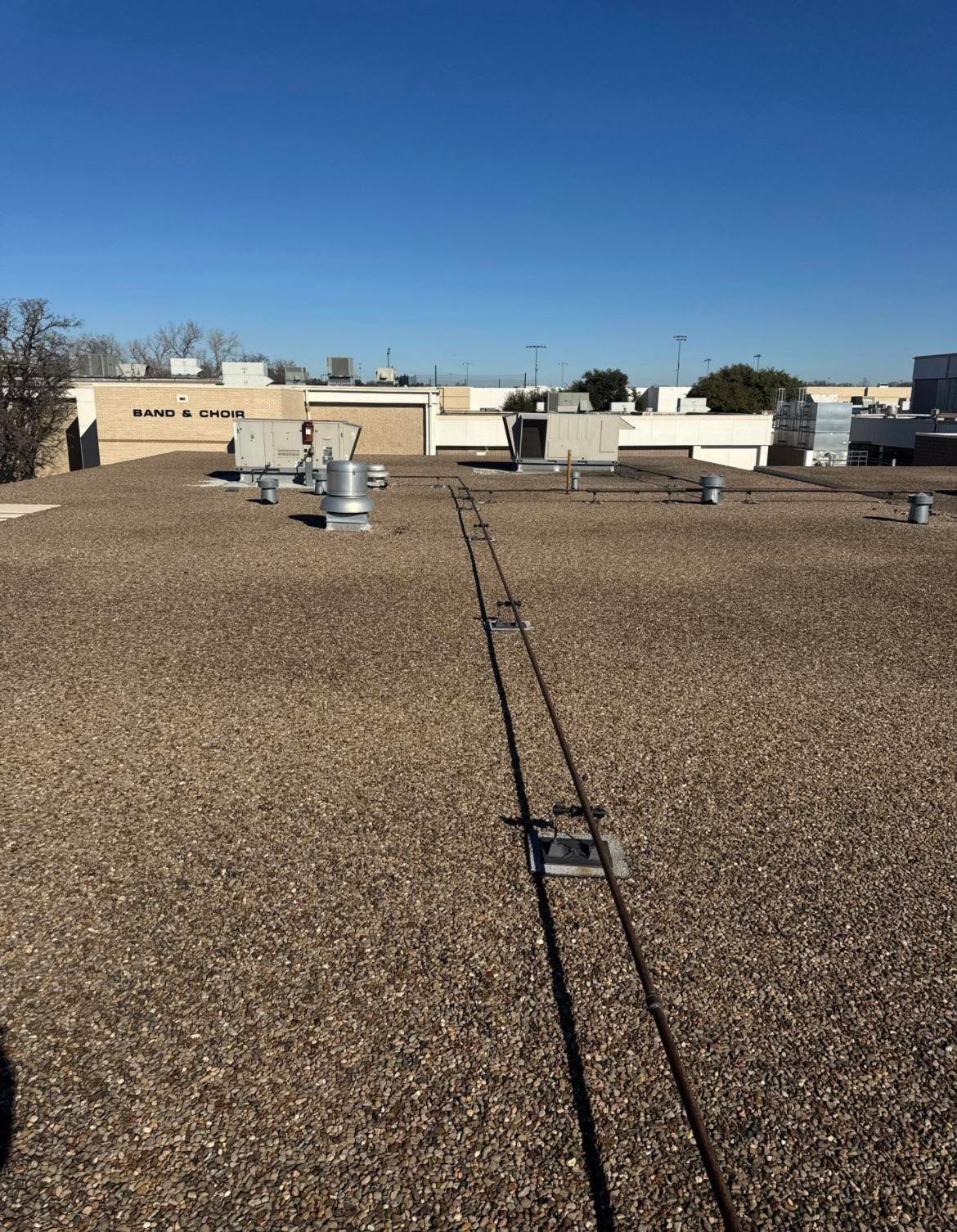 Gravel-covered roof with a safety cable and HVAC units under a clear blue sky.