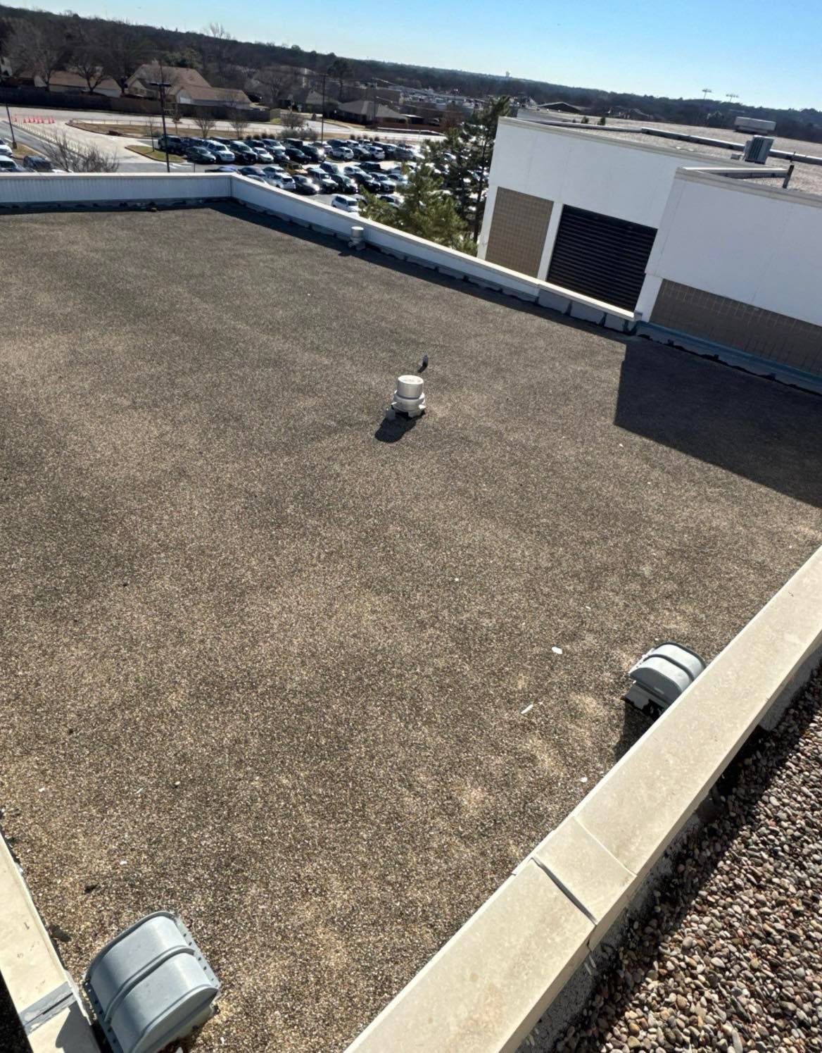 Flat commercial rooftop with HVAC units, gravel surface, and a view of a parking lot.
