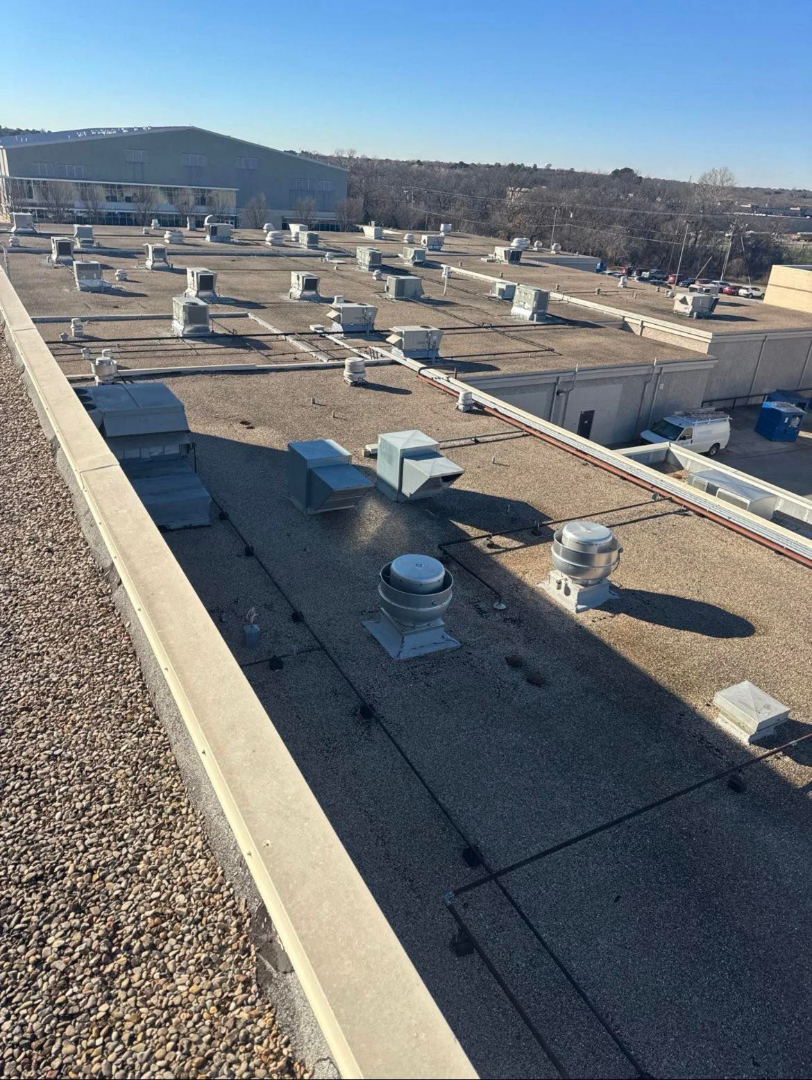 Flat commercial rooftop with vents and gravel perimeter against a clear blue sky.