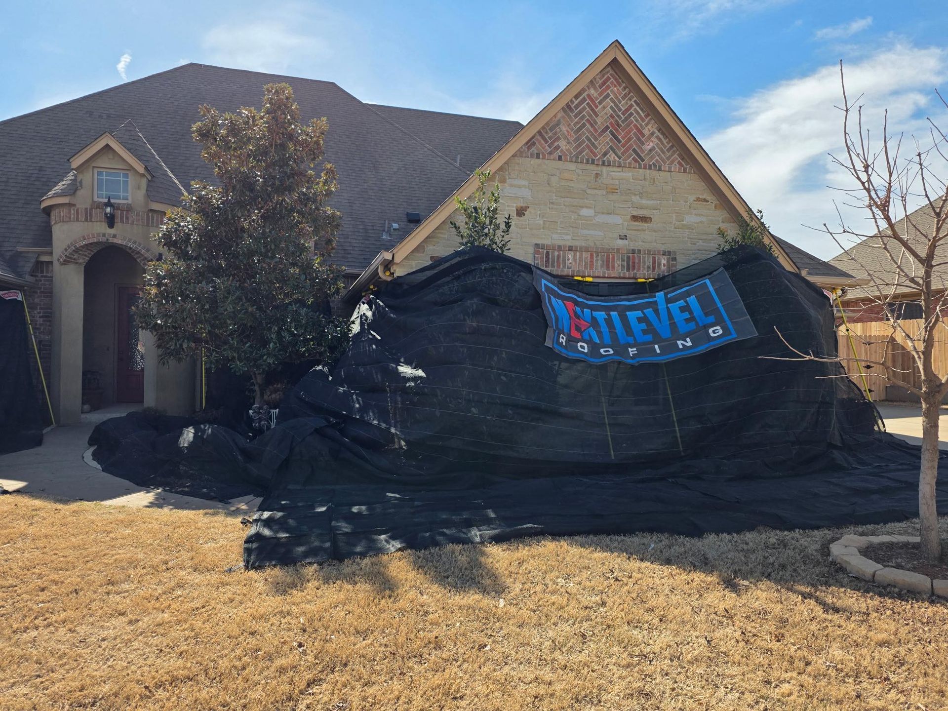 House covered in black tarp for roofing work; blue "Next Level Roofing" sign.